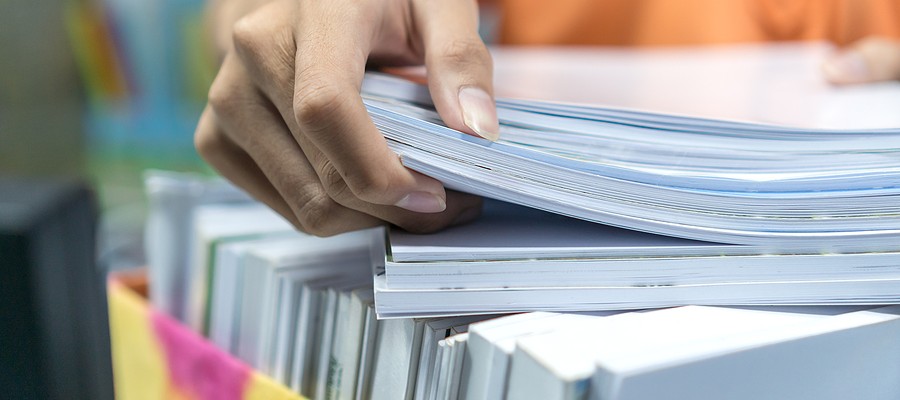 An office worker places a stack of documents onto a box filled with papers and folders.